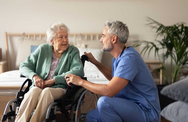An older adult being welcomed by staff in a comfortable assisted living common area.