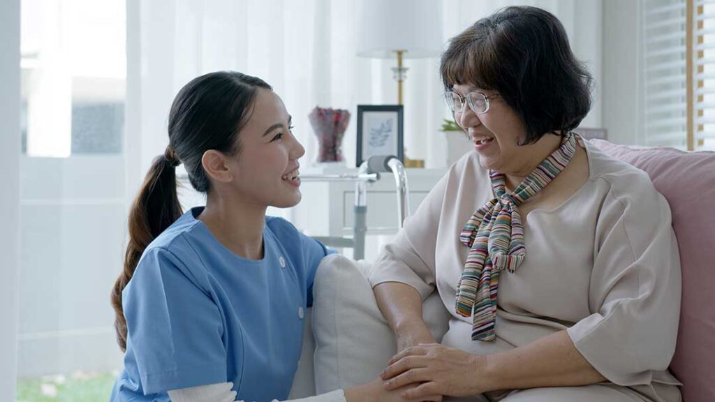 Resident and family member talking in a bright assisted living lounge with visitor sign-in materials nearby