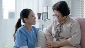 Resident and family member talking in a bright assisted living lounge with visitor sign-in materials nearby